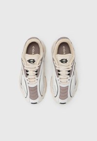 Παπούτσια που συνδυάζουν μπεζ δίχτυ και δέρμα, με σκούρες καφέ λεπτομέρειες. Παχιά σόλα και κορδόνια σε ουδέτερο χρώμα. Το λογότυπο εμφανίζεται σε έντονη θέση.