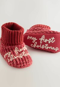 Vermiljoen gebreide sloffen met een geribde boord, met witte tekst die "mijn eerste Kerstmis" zegt. Zachte textuur en warm ontwerp.
