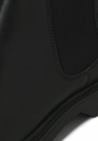 Botas de cuero negro con panel lateral elástico, acabado suave, costuras en contraste a lo largo de la suela y diseño de punta redonda.