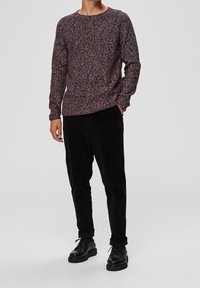 Texturovaný mahagonový svetr s dlouhými rukávy a kulatým výstřihem; spárovaný s černými kordurové kalhotami a černými šněrovacími botami. Klasický neformální outfit.