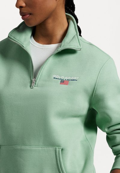 Zaļš flīsa ceturtdaļas-zips pulovers, kas rotāts ar izšuvumu "Polo Sport" logo un ASV karogu. Mīksta tekstūra ar sānu kabatām.