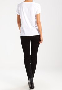 Camiseta blanca de manga corta con mangas enrolladas, combinada con jeans negros ajustados y botas negras de tacón. Diseño minimalista, textura suave.