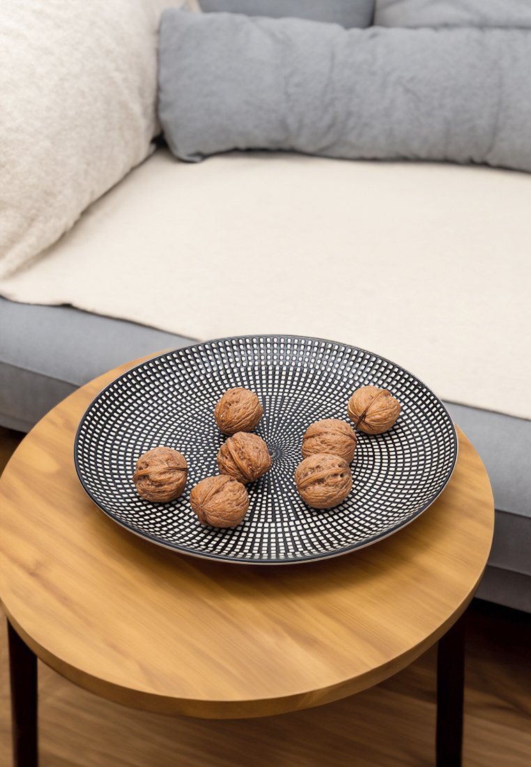 Cuenco de cerámica negra con un patrón de puntos, que contiene ocho nueces enteras, colocado sobre una mesa redonda de madera con acabado liso.