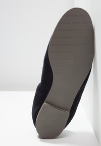 Semelle d'une chaussure de couleur foncée appuyée contre une surface blanche, montrant la marque "Kennel & Schmenger" embossée sur la semelle.