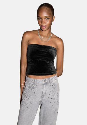 Zwarte fluwelen strapless top gecombineerd met grijze denim jeans met studs bij de zakken. Soepele textuur en een getailleerd ontwerp.