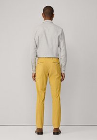 Harmaa pitk�ähihainen paita yhdistettynä kirkkaan keltaisiin kapealahkeisiin housuihin. Housuissa on takataskut vetoketjuilla. Ruskeat kengät täydentävät asukokonaisuutta.