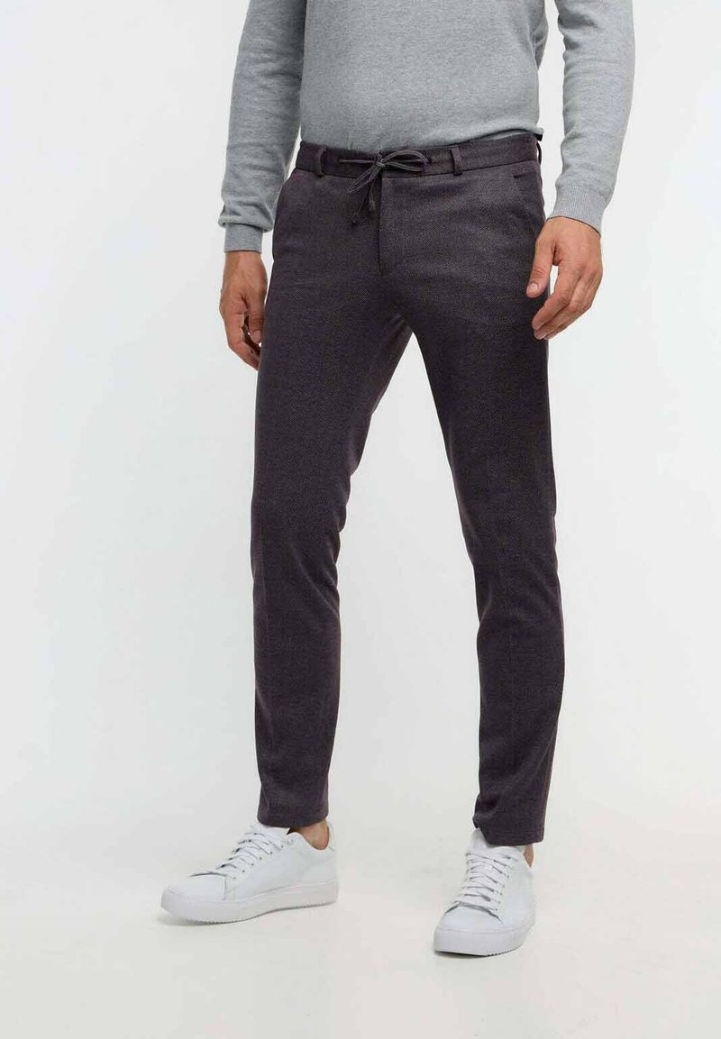 Donkergrijze broek van een gestructureerde stof, met een trekkoord in de taille, slim fit en zijzakken, gecombineerd met witte sneakers.