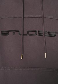 Detailní záběr na fialovou mikinu s kapucí s černým vyšitým logem "SNIPES" a odpovídajícími šňůrkami se metalovými konci.