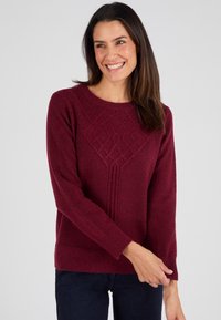 Maglione a maglia bordeaux con un motivo a diamante testurizzato, scollo rotondo e maniche lunghe, abbinato a jeans blu scuro.
