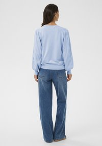 Hele sinine pullover soonikkoes õhuliselt laienevate varrukatega, kombineeritud laia säärega siniste teksadega. Komplekt on mugava lõike ja pehme tekstuuriga.