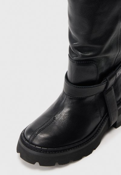 Μαύρη δερμάτινη μπότα έως τον αστράγαλο με στρογγυλή μύτη, καμπύλες ραφές και επίπεδη, υφή καουτσούκ σόλα. Διαθέτει λεπτομέρεια με λουρί κοντά στον αστράγαλο.