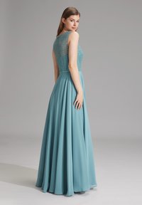 Pitkä, virtaava vaate pehmeässä teal-värissä, jossa on helmilla koristeltu päällinen ja läpinäkyvä päällyste sekä sileä hame, joka laskeutuu elegantisti lattiaan.