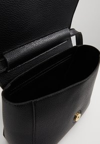 Czarna skórzana torba na ramię o teksturowanym wykończeniu; posiada złote zapięcie na zatrzask i otwarte wnętrze. Projekt jest minimalistyczny i funkcjonalny.