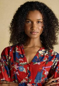 Rotes Blumenkleid mit blauen und rosa Blumen, Knopfdetails und einem V-Ausschnitt. Der Stoff hat eine glatte, seidige Textur.