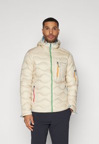 Puffy cream-colored jacket with a hood, featuring zigzag quilting, green zipper, and orange, blue accent zippers on pockets.