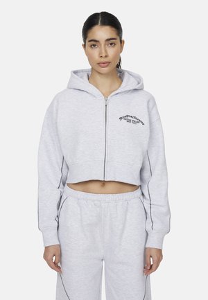 Felpa corta grigia chiara con zip anteriore, cappuccio con cordino e testo ricamato nero. Presenta polsini a costine e dettagli cuciti sui lati.
