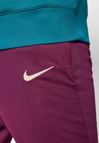 Nike urheilupaita teal- ja purppurakankaasta, jossa on sileä pinta ja voimakas logo vaniljavärillä purppurakohdassa.