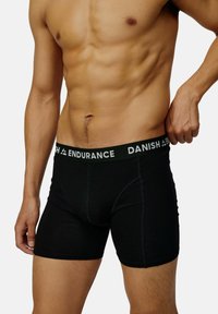 Boxer-briefs noirs avec une large ceinture noire portant le texte blanc "DANISH ENDURANCE." Le matériau semble doux avec une texture lisse.