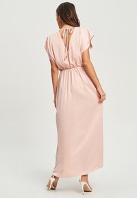 Maxi dress in soft pink fabric with a cinched waist, flutter sleeves, and a keyhole back tied with a ribbon. Smooth, flowing texture.