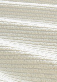 Tessuto bianco testurizzato con strisce a coste in rilievo alternate a linee lisce, creando un motivo sottile e una superficie tattile.