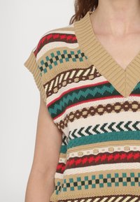 Suéter de punto de manga corta con escote en V, patrones multicolores en verde, rojo, marrón y crema, con un cuello acanalado y texturizado.