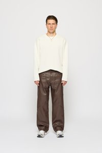 Top blanco de manga larga con escote en V, combinado con pantalones de piel sintética marrones con costuras decorativas. Zapatillas ligeras completan el atuendo.