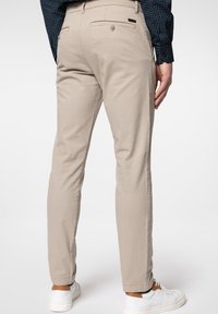 Beiga byxor med slim fit, i bomullsmaterial, två bakfickor och en liten logotagg. Bärs tillsammans med vita sneakers och en mönstrad skjorta.