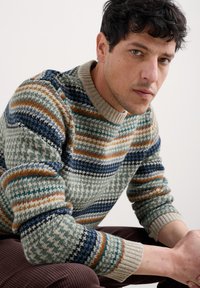 Gestrickter Pullover im mehrfarbigen Muster mit grünen, blauen, orangefarbenen und cremefarbenen Nuancen. Rippkragen und -säume, ausgeprägte geometrische Designs.