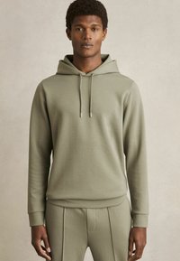 Hoodie in gedempt olijfgroen, met een eenvoudig ontwerp, zachte textuur, elastische manchetten en subtiele trekkoordaccenten.
