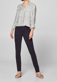 Camisa de botones a rayas en blanco y gris, con dos bolsillos en el pecho; combinada con jeans skinny oscuros y sandalias de tacón rosa claro.