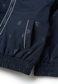 Rompevientos azul marino con textura suave, que presenta un patrón sutil, puños elásticos, cierre de cremallera y dos bolsillos laterales.