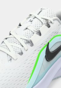 Zapatilla deportiva blanca con parte superior de malla, presenta el logotipo negro de Nike, detalles en azul claro y verde neón, y suela texturizada para mayor agarre.