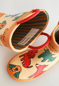 Gummistiefel mit einer cremefarbenen Basis, die bunte Hundemotive in Rot, Grün und Orange zeigen. Sie haben rote Griffe und ein gestreiftes Innenfutter.