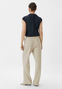 Marineblauwe blouse met geplooide achterkant, gecombineerd met beige wijde broek. De outfit heeft een gladde textuur en een getailleerde pasvorm.