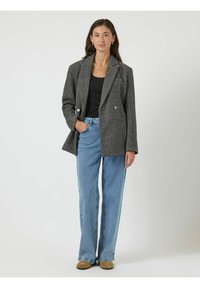 Grijze houndstooth-blazer met dubbele knoopsluiting, brede revers en twee knopen, gecombineerd met lichtblauwe rechte jeans en bruine schoenen.