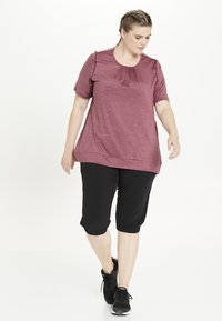 Bordeaux kortärmad topp med en sammanknuten halsringning, i kombination med svarta capribyxor med elastiska mudd och svarta träningsskor.