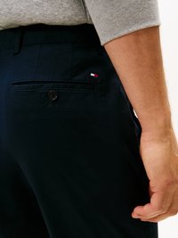Pantaloni blu navy con una texture liscia, dotati di una tasca posteriore con un bottone nero e un piccolo logo nei colori rosso, bianco e blu.