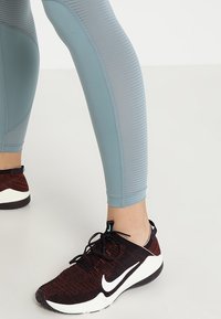 Leggings deportivos azul claros con textura acanalada y diseño ajustado, combinados con zapatillas negras y rojas que presentan un swoosh blanco.