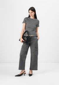 T-shirt às riscas preto e branco combinado com calças cargo cinzentas com bolsos laterais e um corte descontraído. Acessorizado com uma pequena mala preta e sapatos de bico.