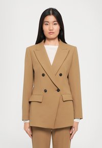 Dobbeltradet blazer i en varm kamelfarge. Laget av glatt stoff, har den spisse klaffer, svarte knapper og frontlommer med klaff.