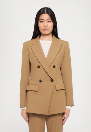 Dobbeltradet blazer i en varm kamelfarge. Laget av glatt stoff, har den spisse klaffer, svarte knapper og frontlommer med klaff.