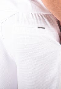 Shorts blancs texturés avec un motif en mesh, une taille élastique et une petite poche avec une étiquette en métal.