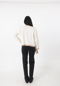 Maglione cropped color crema con orlo taupe, indossato con jeans neri a gamba dritta. Tessuto liscio, design semplice, maniche lunghe.
