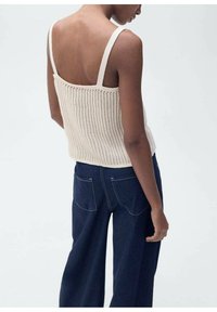 Pletený top bez rukávů v odstínu off-white s texturovaným žebrovaným vzorem a tenkými ramínky; doplněný o tmavě modré široké džíny se zadními kapsami.