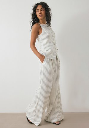 White striped sleeveless top with buttons paired with wide-leg striped trousers. Fabric has a smooth texture. Features slanted pockets.