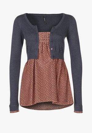 Cardigan lavorato a maglia blu navy indossato sopra una camicetta floreale a fantasia nei toni pesca e nero. Presenta bottoni e un orlo svasato.