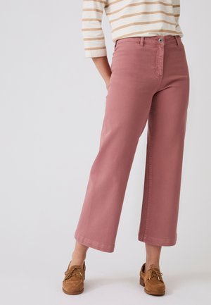 Persona che indossa pantaloni rosa a gamba larga tagliati, scarpe marroni con lacci e una maglia a righe beige e bianca a maniche lunghe.