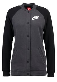 Grå och svart Nike-jacka i jersey med knäppning framtill, sidofickor och logotyp på vänster bröst. Tillverkad av ett mjukt tyg med en slät yta.