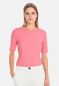 Short-sleeve, round-neck top in bright pink, made of smooth fabric. Paired with white pants featuring a button detail.