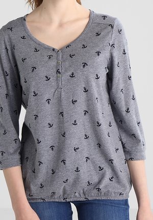 Chemise grise à manches longues avec motifs d'ancre noirs et un col henley à trois boutons portée avec un jean bleu.